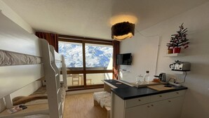Una habitación acogedora con literas, un pequeño kitchenette, una ventana con vistas a montañas nevadas y un televisor montado.