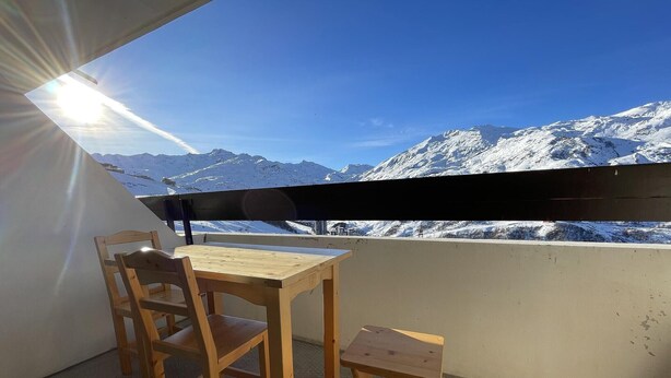 Una mesa y sillas de madera en un balcón con vistas a montañas nevadas.