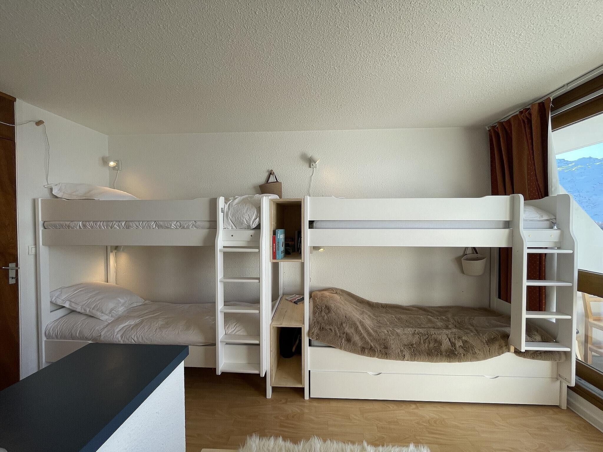 A room with bunk beds, a desk, and a window with curtains.