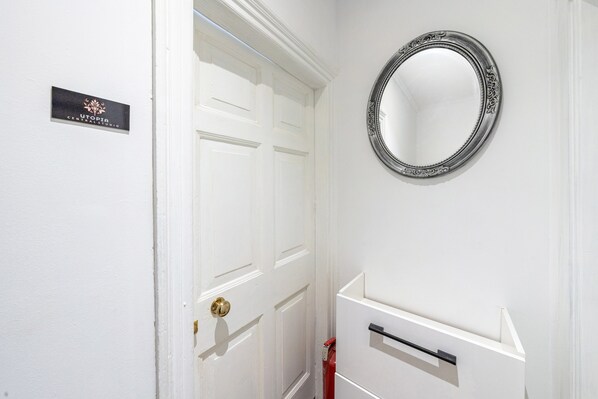 A white door with a brass doorknob, a black sign with gold lettering, and a round mirror with an ornate frame.
