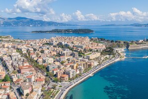 Vista aérea de una ciudad costera con densa construcción urbana, un destacado paseo marítimo y una isla distante.