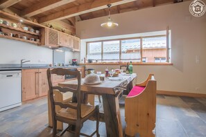 Una cocina con armarios de madera, una mesa de comedor con sillas y una ventana con vista a un edificio.