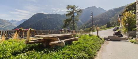 A scenic mountain view with a wooden bench, a stone wall, and a road.