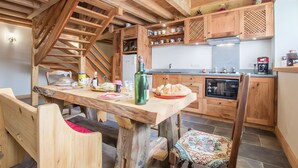 Una cocina rústica con vigas de madera, una mesa de comedor, sillas y una escalera.