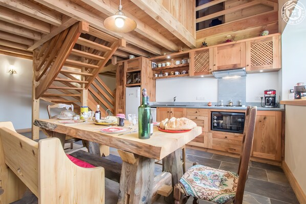Una cocina rústica con vigas de madera, una mesa de comedor, sillas y una escalera.