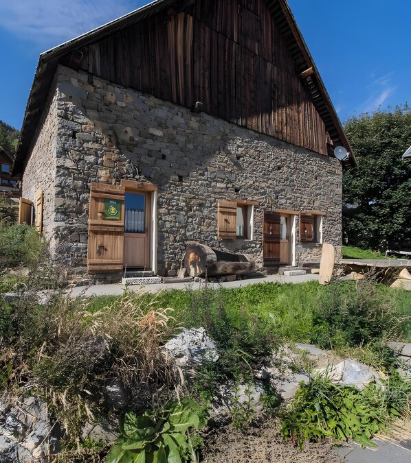 A stone building with wooden doors and windows, a satellite dish, and a stone staircase leading to the entrance. - Apartment 'Le Blanchon' with Mountain View and Wi-Fi (Montricher-Albanne)