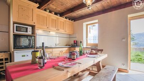 A kitchen with wooden cabinets, a dining table set with red tablecloth, and a view of the outdoors.