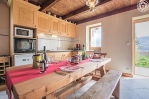 A kitchen with wooden cabinets, a dining table set with red tablecloth, and a view of the outdoors.
