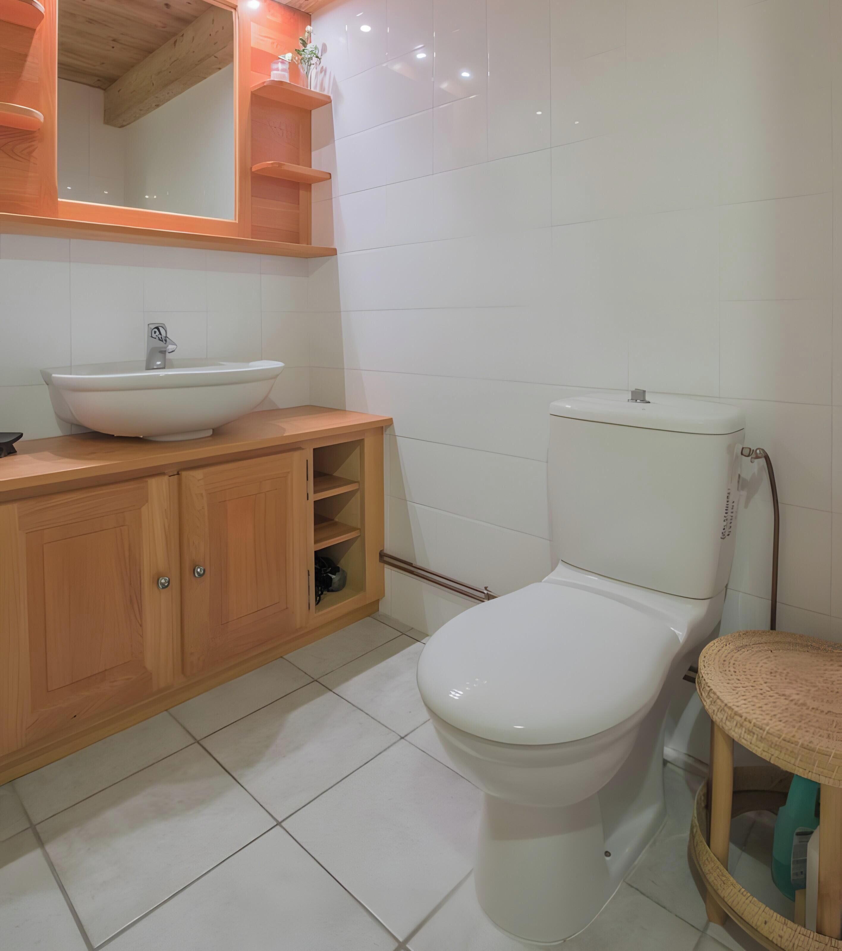 Une salle de bain avec des toilettes blanches, un meuble-lavabo en bois et un miroir au-dessus du meuble-lavabo.