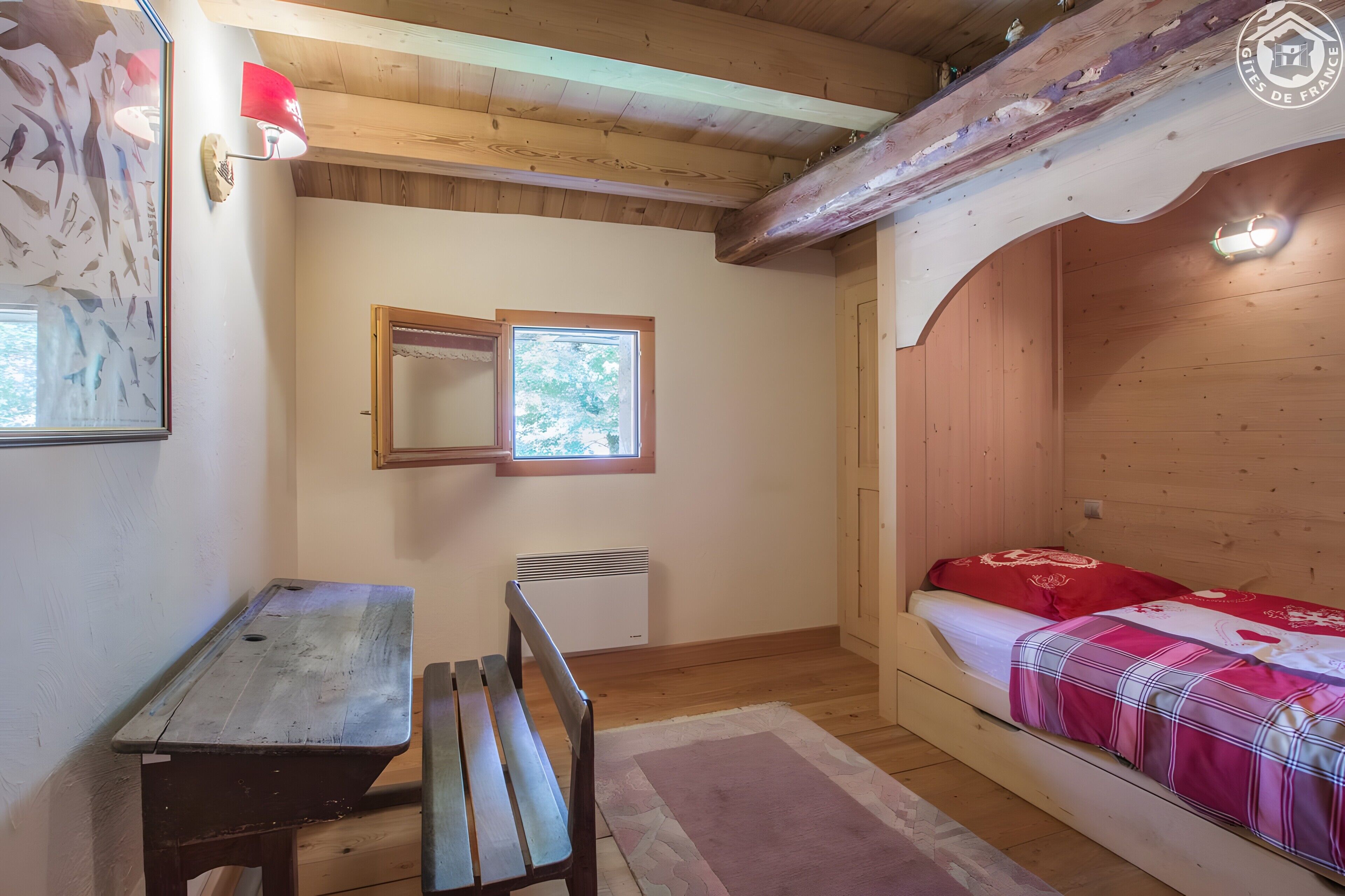 A wooden cabin room with a bed, a bench, a radiator, and a window.