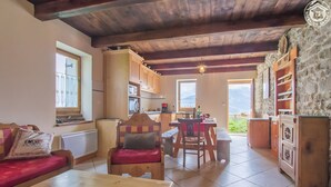 A cozy interior with a wooden ceiling, a dining area, a kitchen, and a view through a window.