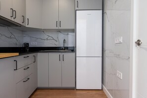 A kitchen with grey cabinets, a black countertop, a white refrigerator, and marble backsplash. - Bright Spacious Apartment with Private Terrace & Air Conditioning in Seville (Seville)