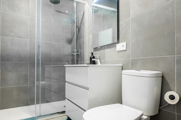 A bathroom with a glass shower enclosure, a white sink, and a toilet.