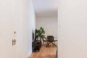 A narrow hallway with a wooden floor, a desk with a computer, a chair, and a potted plant.