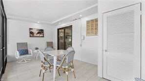 A modern dining area with a glass table and wicker chairs, a small side table with a plant, and a painting on the wall. - Canal Dreamin | Heated Pool • Mini Golf • Waterfront Oasis Near Vanderbilt Beach (Naples)