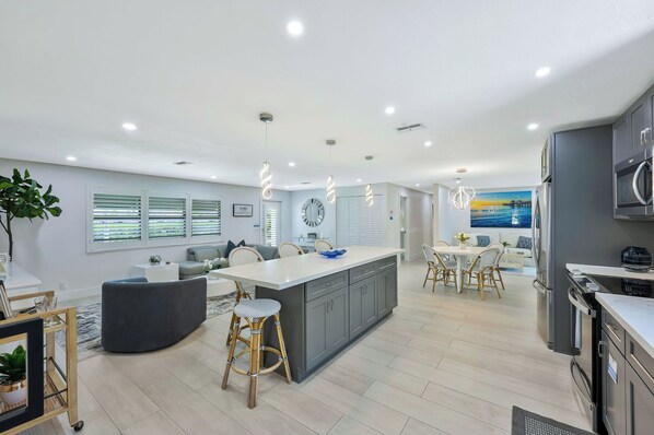 A modern kitchen with a central island, dining area, and a living space with a sofa and coffee table. - Canal Dreamin | Heated Pool • Mini Golf • Waterfront Oasis Near Vanderbilt Beach (Naples)