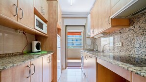 Una cocina estrecha con armarios de madera, un microondas, una lavadora y suelo de baldosas.