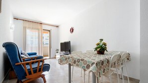 Una sala de estar con un sofá azul, una mesa de comedor con mantel estampado y un televisor.