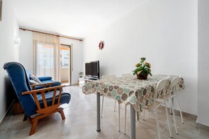 A living room with a blue sofa, a dining table with a patterned tablecloth, and a television.