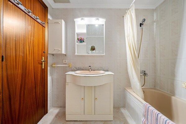 Un baño con puerta de madera, un lavamanos con espejo, una ducha con cortina y un perchero para toallas.