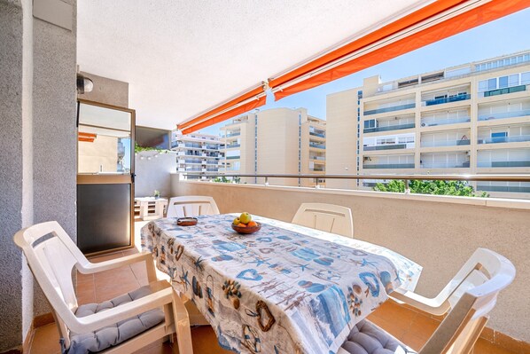 Un balcon avec une table et des chaises, une vue sur les bâtiments et un espace abrité avec un fauteuil.