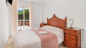 Een slaapkamer met een bed, een houten nachtkastje, een aan de muur bevestigde televisie en een raam met gordijnen.