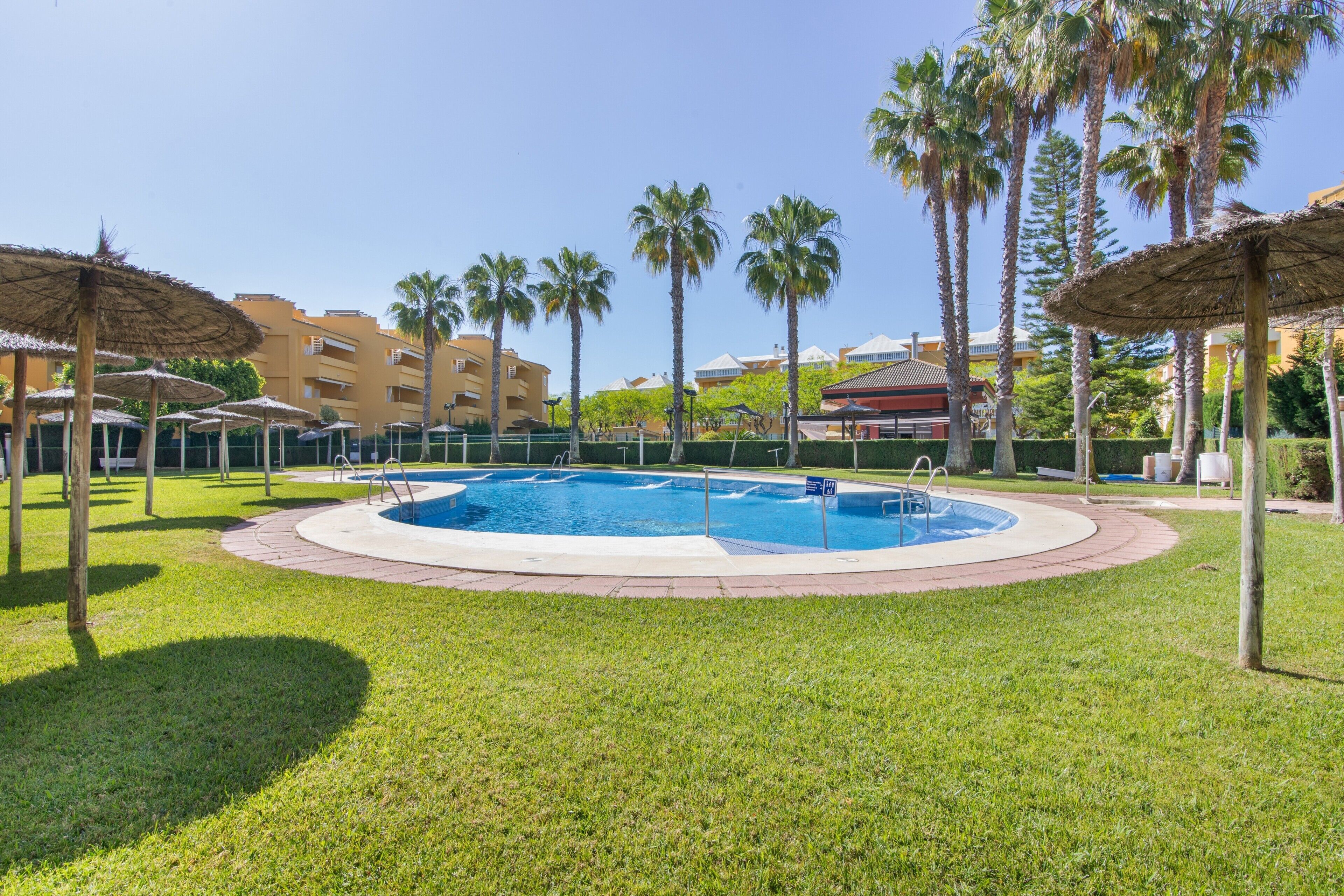 A swimming pool surrounded by palm trees and a building in the background.. Apartment 'Las Arenas' with Shared Pool, Private Terrace and Wi-Fi