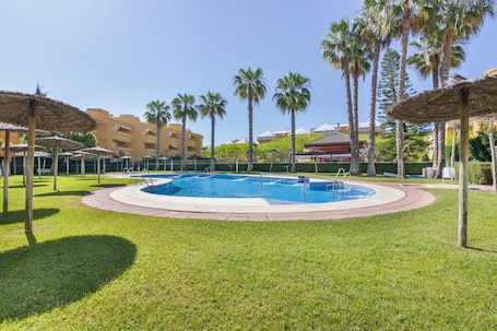 A swimming pool surrounded by palm trees and a building in the background.. Apartment 'Las Arenas' with Shared Pool, Private Terrace and Wi-Fi