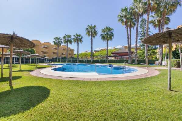 Une piscine entourée de palmiers, avec un bâtiment en arrière-plan.