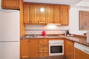 Una cocina con armarios de madera, un refrigerador blanco, un lavamanos, una tetera y un lavavajillas.