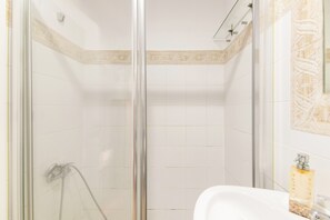 A bathroom with a glass shower enclosure, white tiles, a sink, and a mirror with decorative wall tiles. - Apartment 'Las Arenas' with Shared Pool, Private Terrace and Wi-Fi (Islantilla)