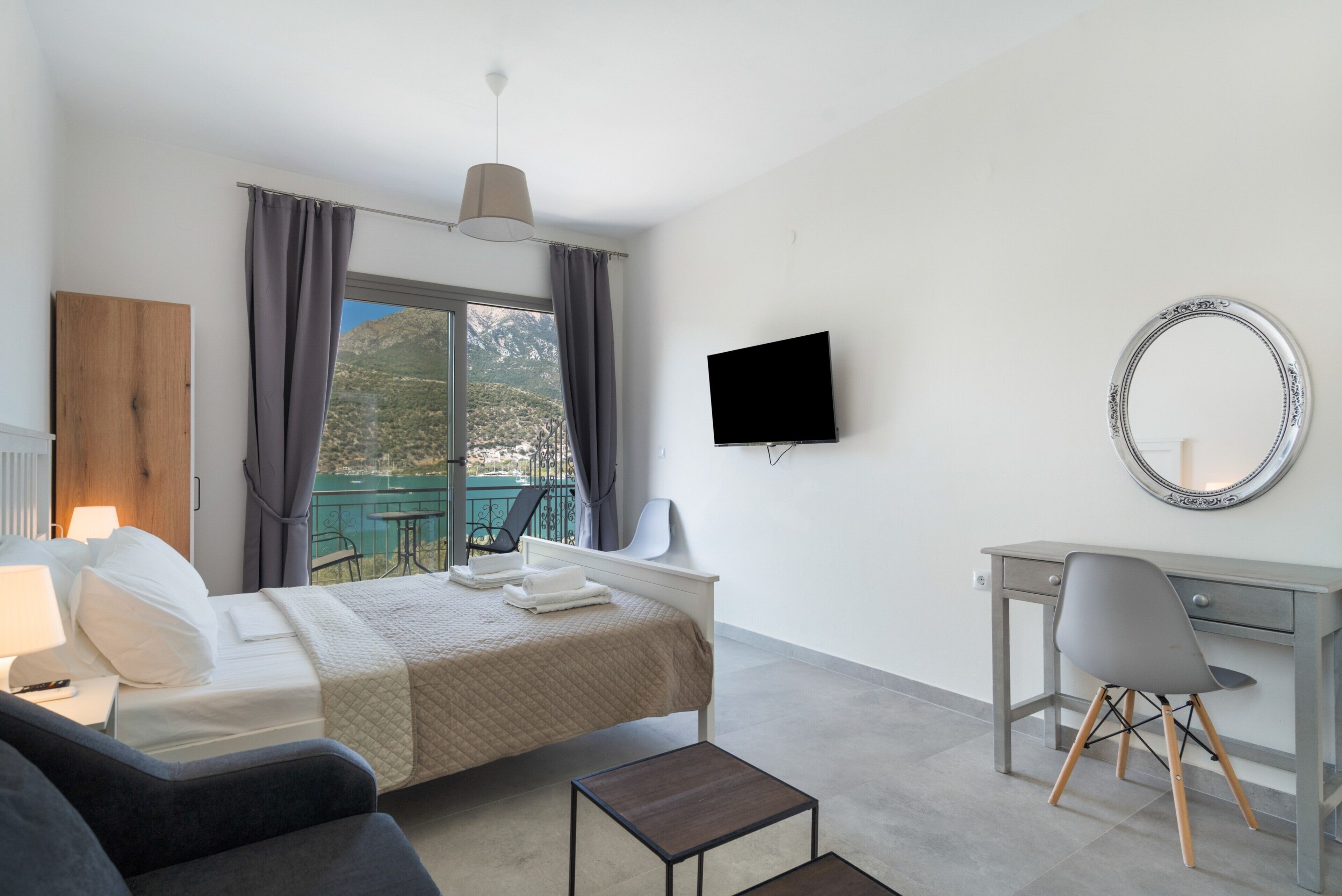 A hotel room with a bed, a desk, a chair, a TV, and a balcony with a view of mountains.