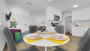 Una cocina moderna con armarios blancos, un microondas y un comedor con una mesa redonda y cuatro sillas.