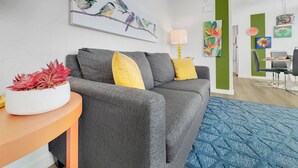 Una sala de estar moderna con un sofá gris, cojines amarillos, un tapete azul y una obra de arte con pájaros.