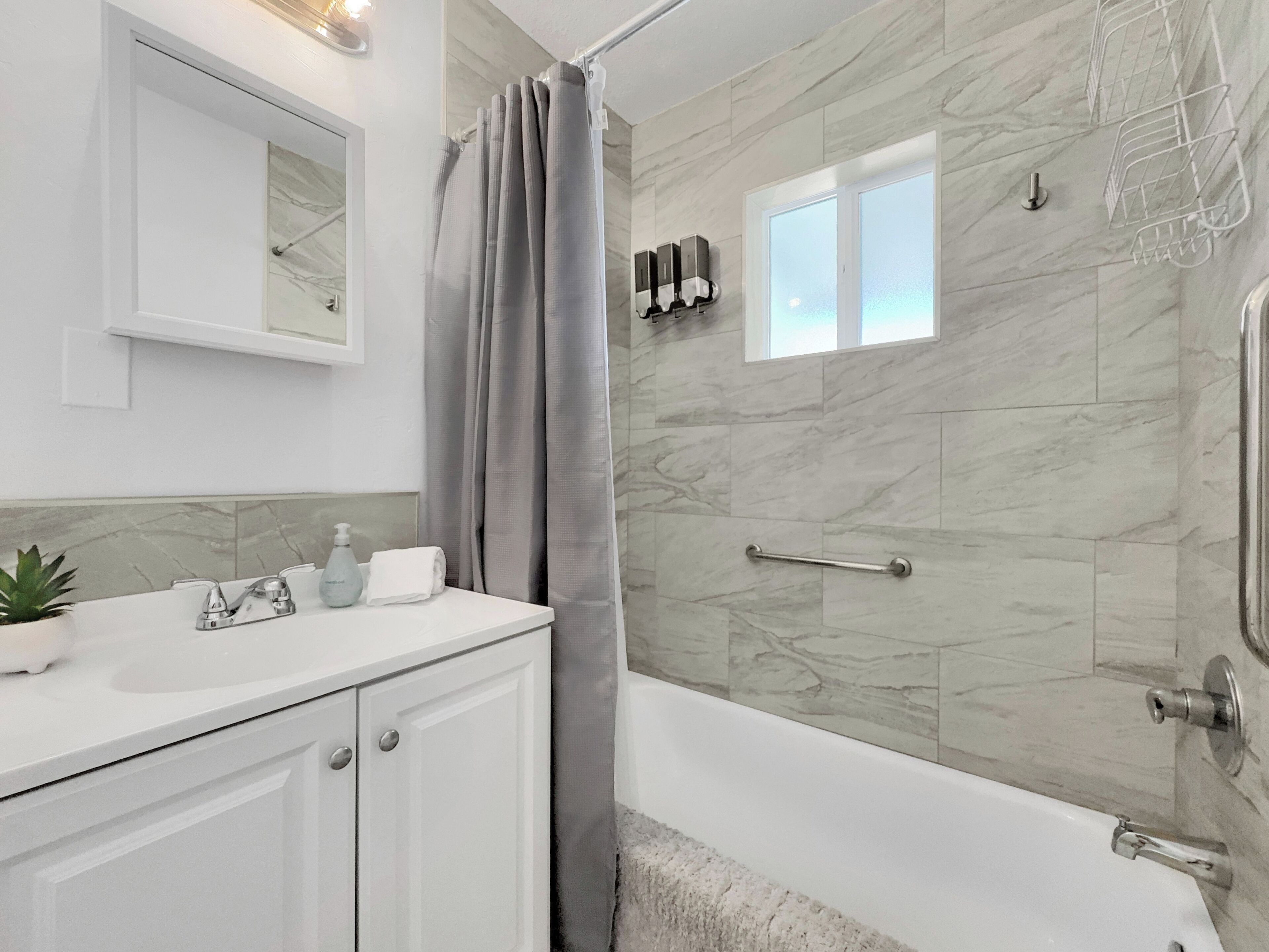 Un baño moderno con pared de ducha de mármol, bañera y tocador con espejo y planta.