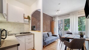 A modern kitchen with white cabinets, a gas stove, and a sink. There is a dining area with a gray sofa and a table with chairs. - Apartment 'Modern Park' with Shared Garden, Balcony and Wi-Fi (Meran)