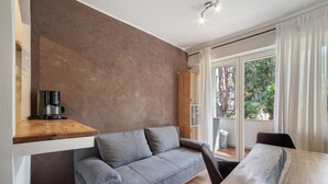 A modern living room with a grey sofa, a wooden coffee table, and a large window with a view of greenery. - Apartment 'Modern Park' with Shared Garden, Balcony and Wi-Fi (Meran)