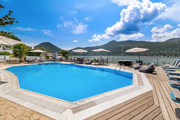 Una piscina con sillones de descanso y sombrillas, rodeada de montañas.