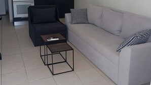 A modern living room with a grey sofa, a black armchair, and a coffee table. There is a kitchen area with a microwave and oven. - Apartment 'Chakalaka -  2 Bedrooms 5' with Sea View, Wi-Fi and Air Conditioning (Leykada)