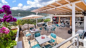 An outdoor patio with tables and chairs, a bar area, and a view of the sea and mountains. - Apartment 'Chakalaka -  2 Bedrooms 5' with Sea View, Wi-Fi and Air Conditioning (Leykada)