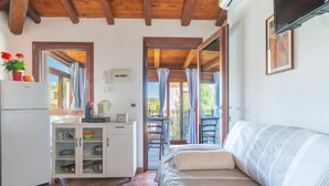A cozy room with a bed, a small kitchenette, a dining area, and a balcony with curtains.