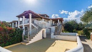 A multi-story building with a covered outdoor area, a staircase, and a sandy courtyard.