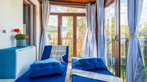 A balcony with two blue beds, a potted plant, and a view of the surrounding area.