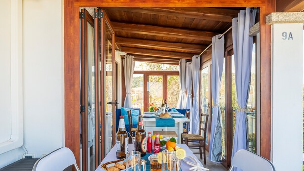 A covered outdoor dining area with a table set for two, featuring a variety of drinks and snacks.