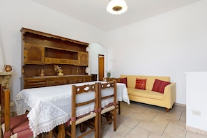 A dining area with a wooden table and chairs, a yellow sofa, and a cabinet with shelves. - Apartment 'Un Oasi Di Tranquillità' with Mountain View, Private Garden and Wi-Fi (San Michele)