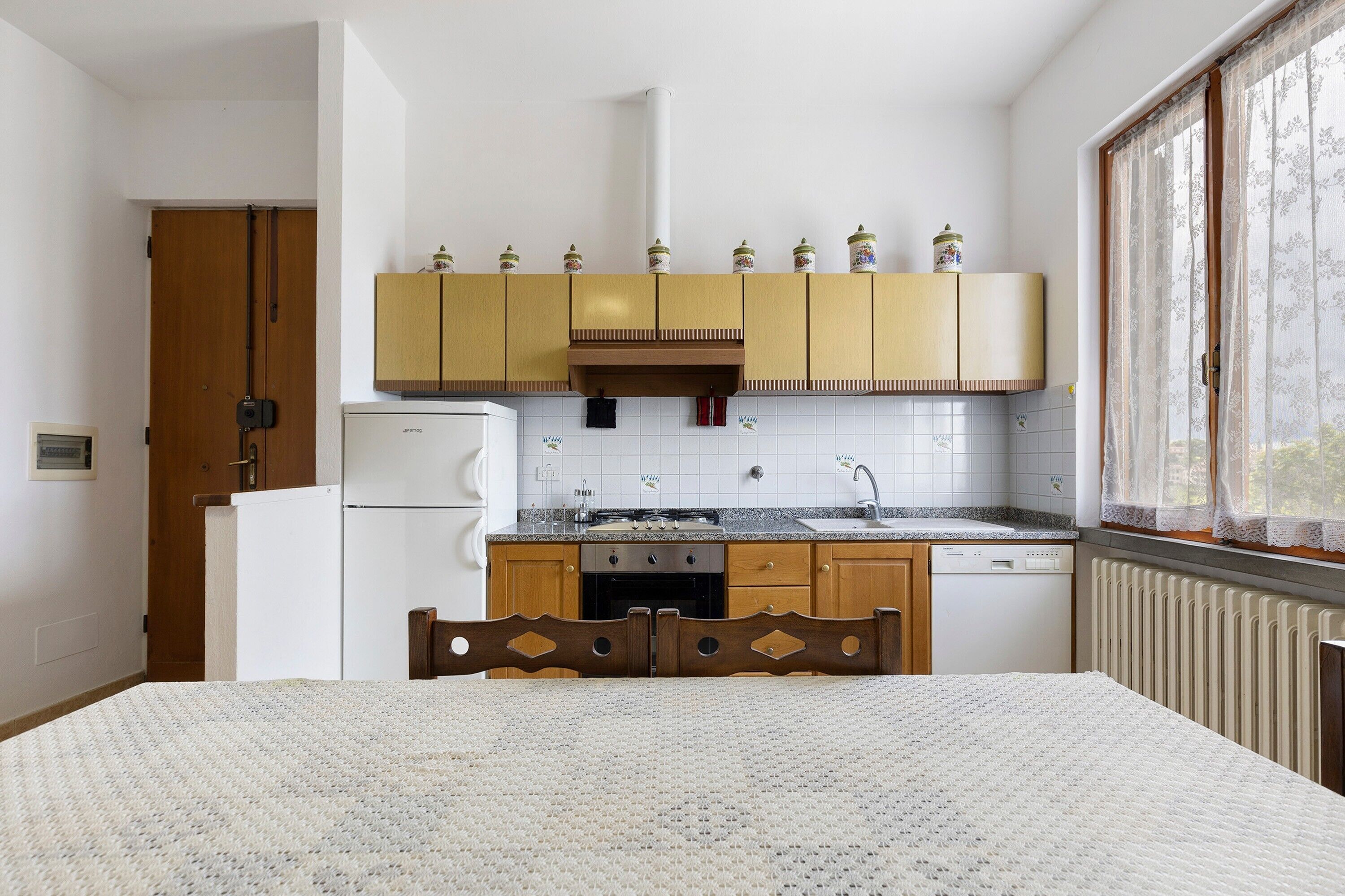 Une cuisine avec des meubles de rangement en bois, un réfrigérateur, une cuisinière et une fenêtre avec des rideaux.