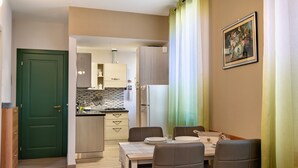 Een kleine keuken met moderne apparaten, een eethoek met een tafel en stoelen, en een groene deur die naar een andere kamer leidt.