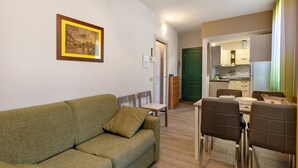 Een woonkamer met een bank en stoelen, een eethoek met een tafel en stoelen, en een keuken op de achtergrond.