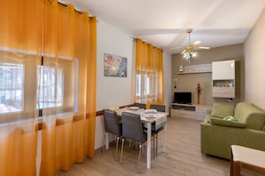 A dining area with a table set for four, a green sofa, and a television in the background.