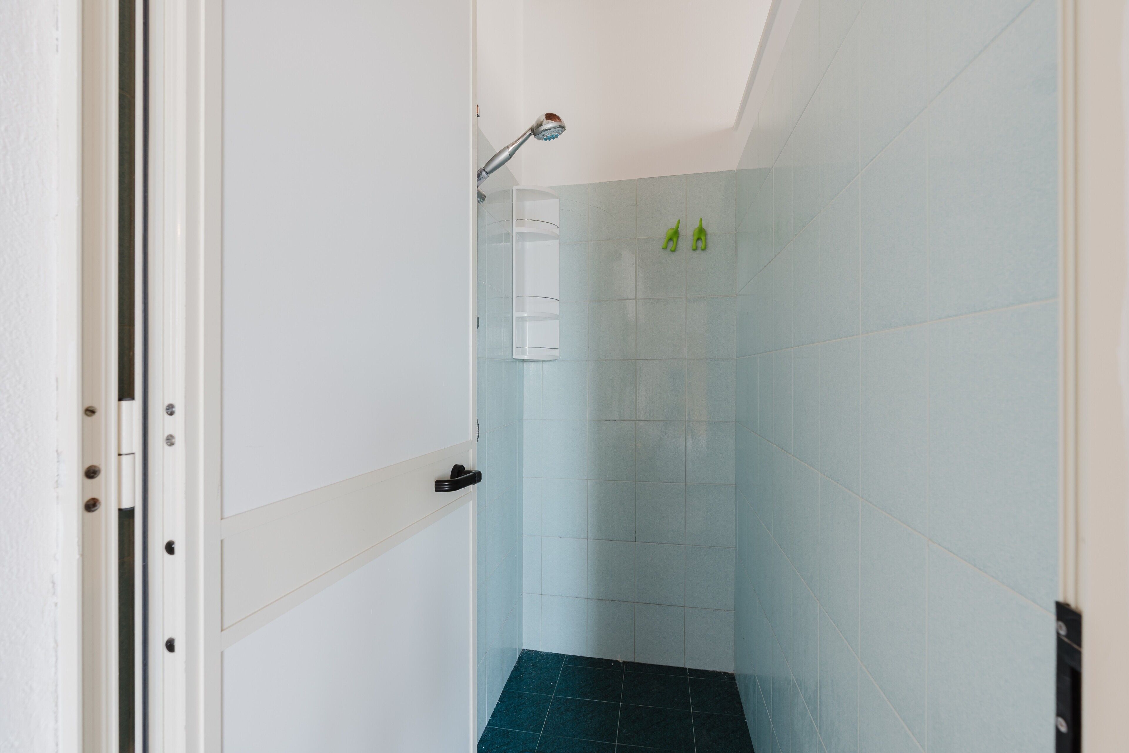 Une salle de bain avec une douche, une porte blanche et un mur carrelé.
